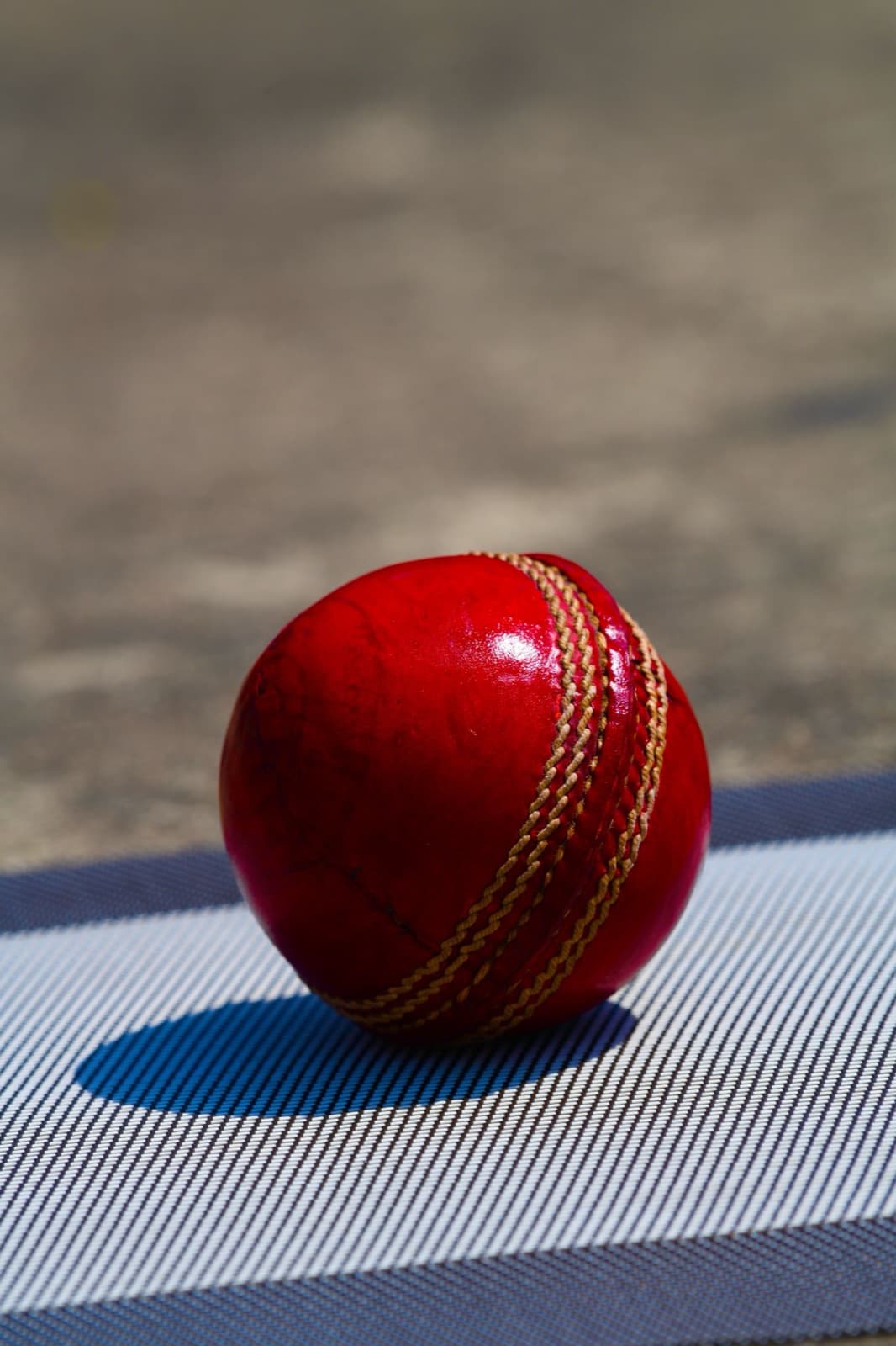 A red cricket ball on a ribbed pitch mat