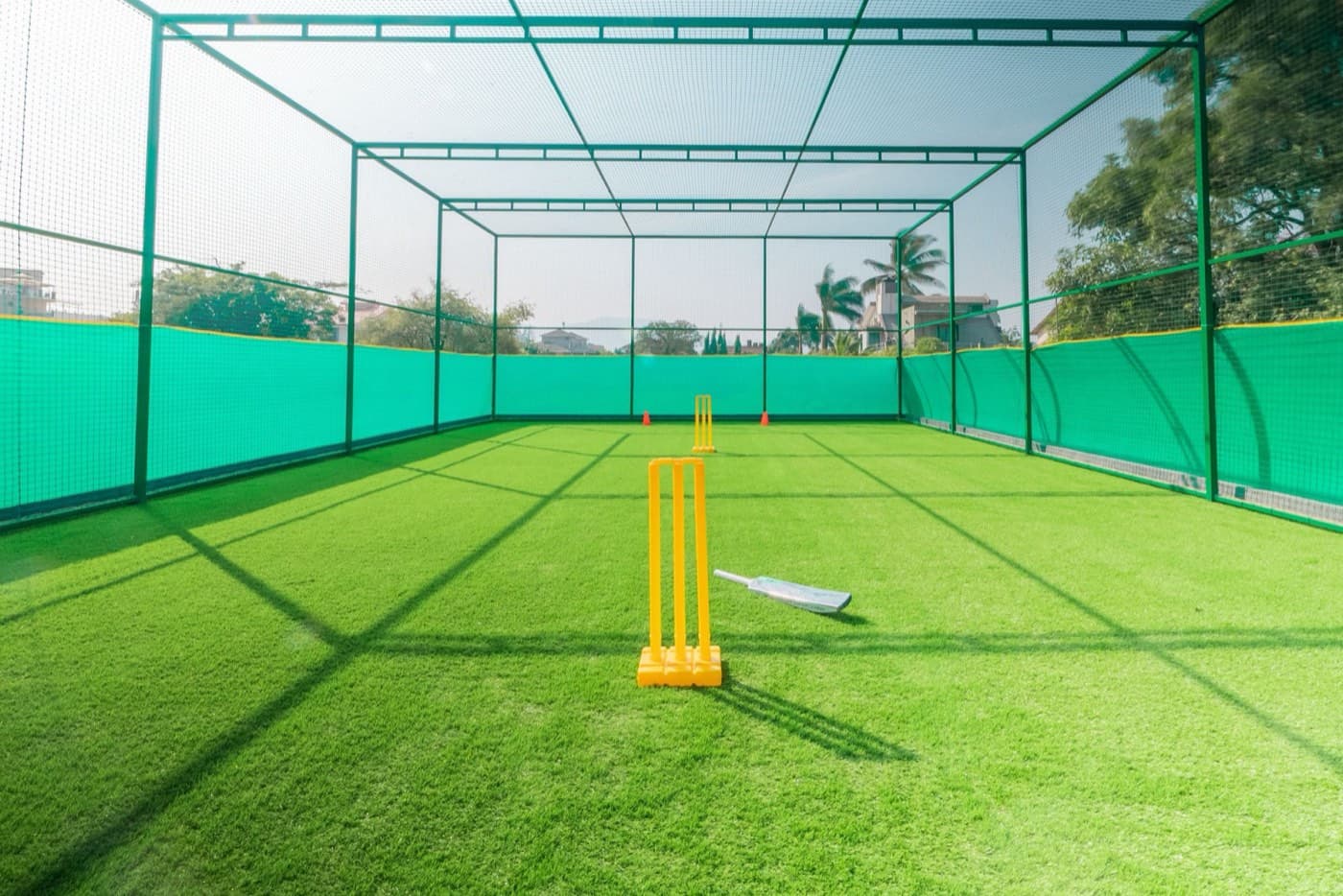 A netted practice lane with stumps and a bat on the turf